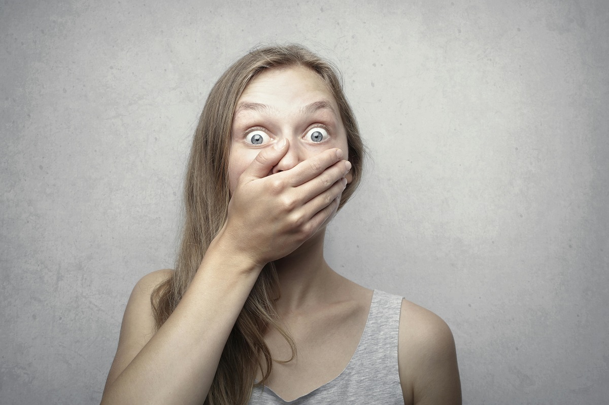 woman with a shocked expression, covering her mouth with one hand